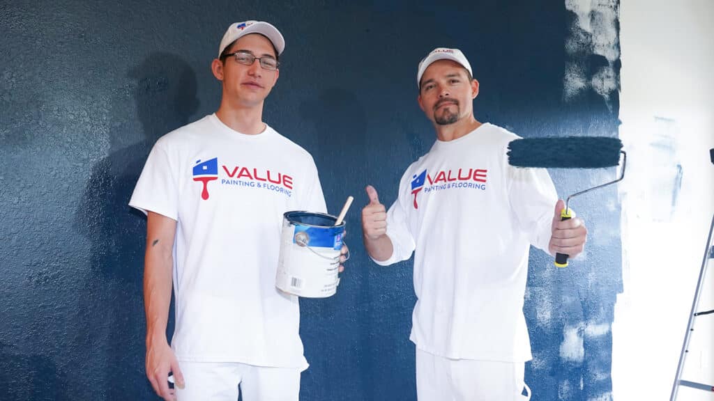 Two workers posing with paintbrush and paint can near a painted wall