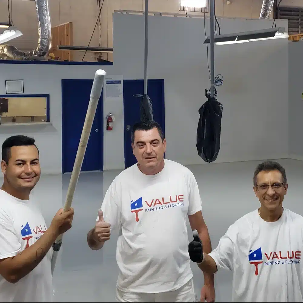 Three cheerful Value Painting workers, all smiles, as they expertly apply epoxy flooring in a commercial space.