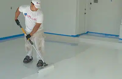 Value Painting and Flooring worker painting a garage floor with expertise