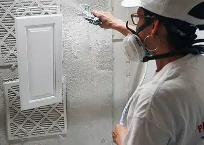 Female worker sprays painting a cabinet door.