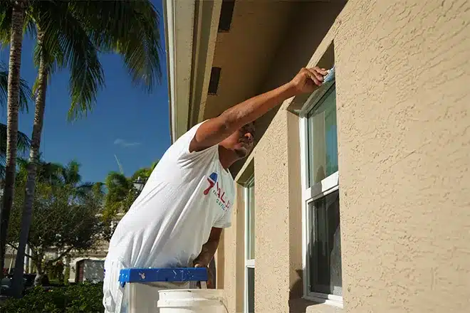 Value Painting and Flooring worker painting the sides near a window.