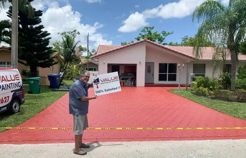 Satisfied customer holding a '100% Satisfied' sign in front of his Florida home walkway that's been abrasive sand blasted and painted by Value Painting and Flooring