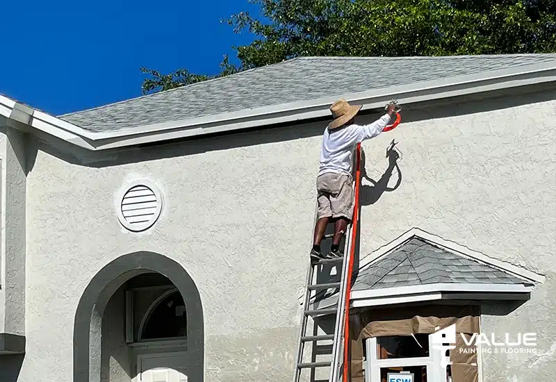 Value Painting and Flooring worker painting a home exterior