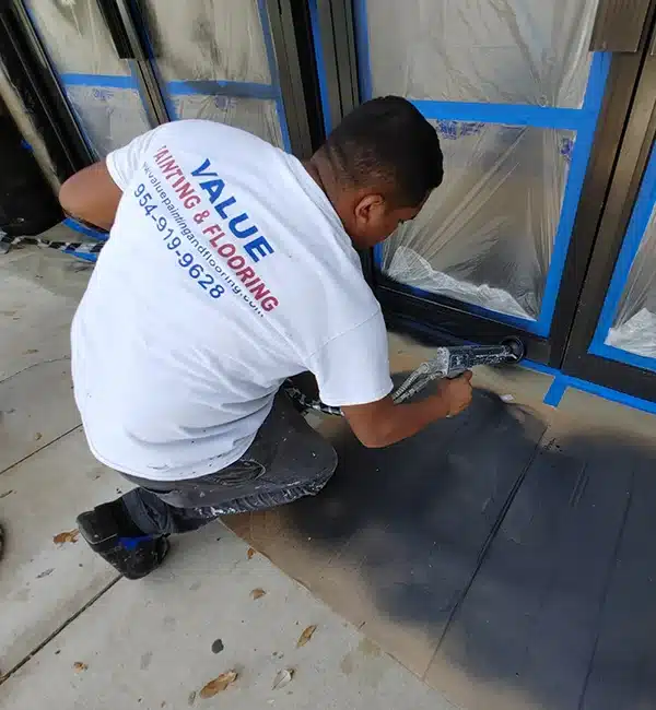 Value Painting and Flooring worker electrostatic spray painting a commercial store's exterior door